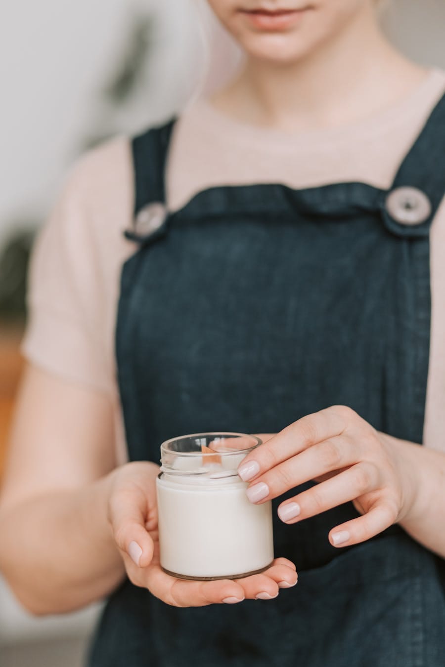 Close-up of a woman holding a handmade candle in a glass jar, emphasizing small business craftsmanship.