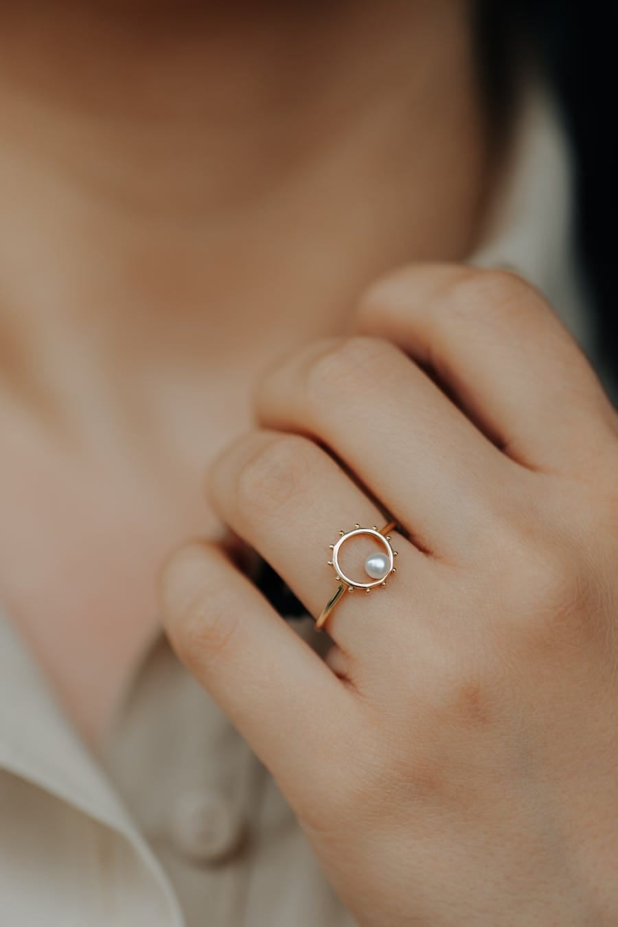 Close-up of a woman wearing a gold ring with a pearl, showcasing elegant jewelry design.