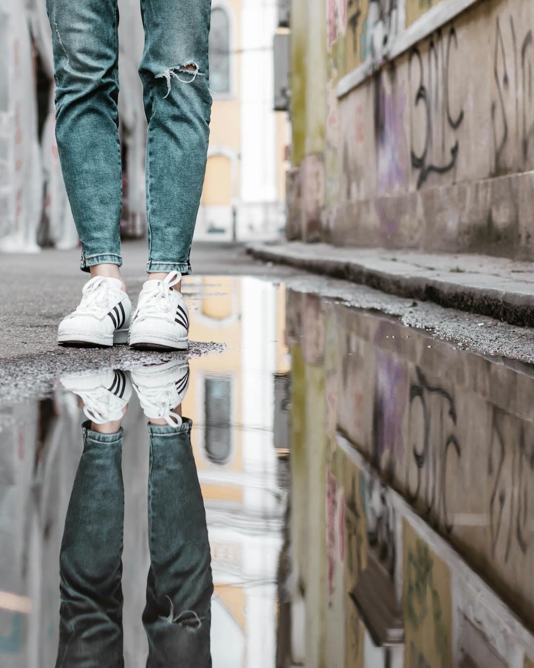 Close-up of sneakers and jeans reflected in a puddle on an urban street, Cluj-Napoca.