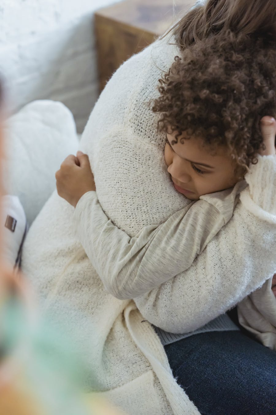 Comforting moment of a mother hugging her child on a cozy couch indoors.