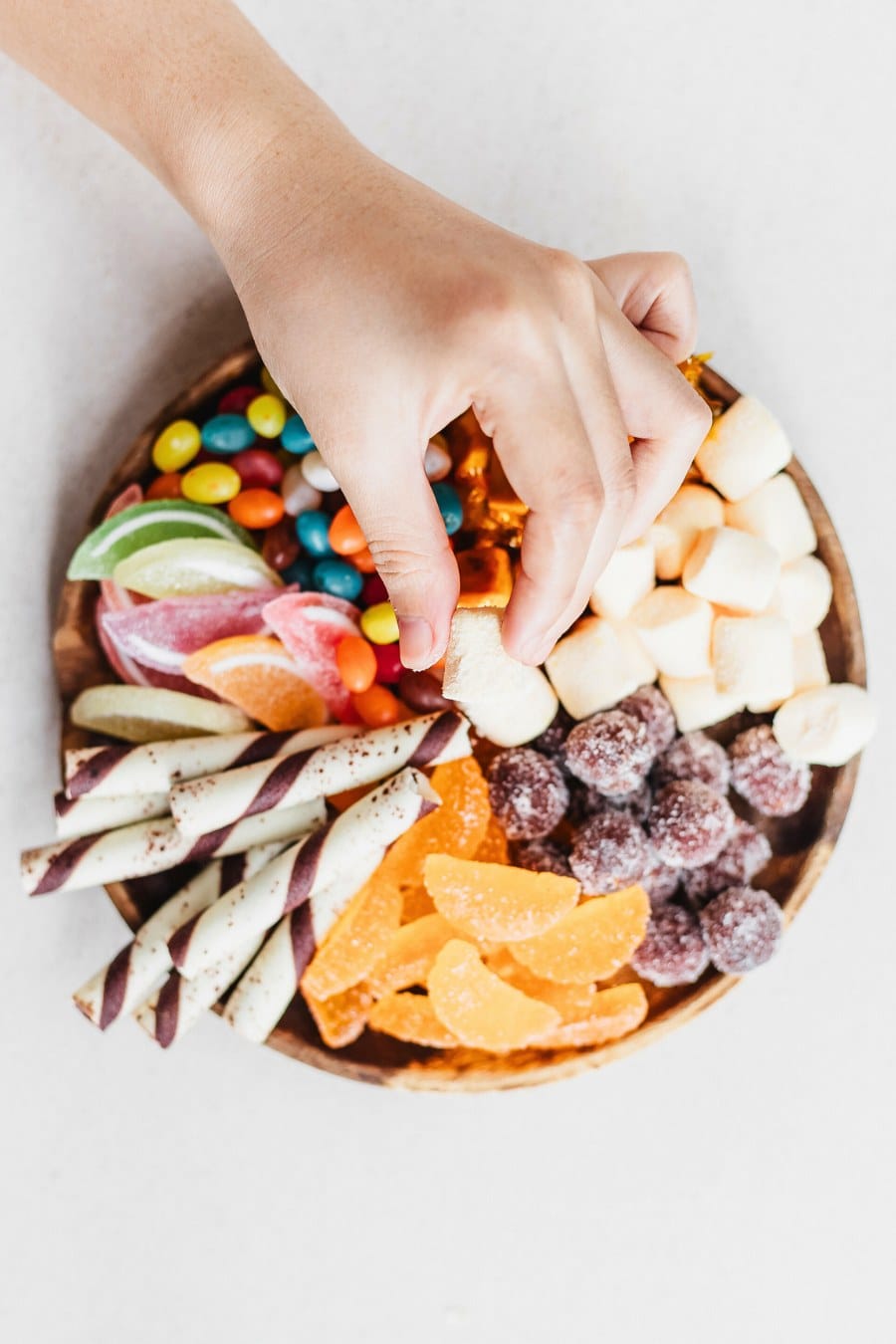 Hand with Marshmallow Above the Plate of Assorted Candy; candy charcuterie board