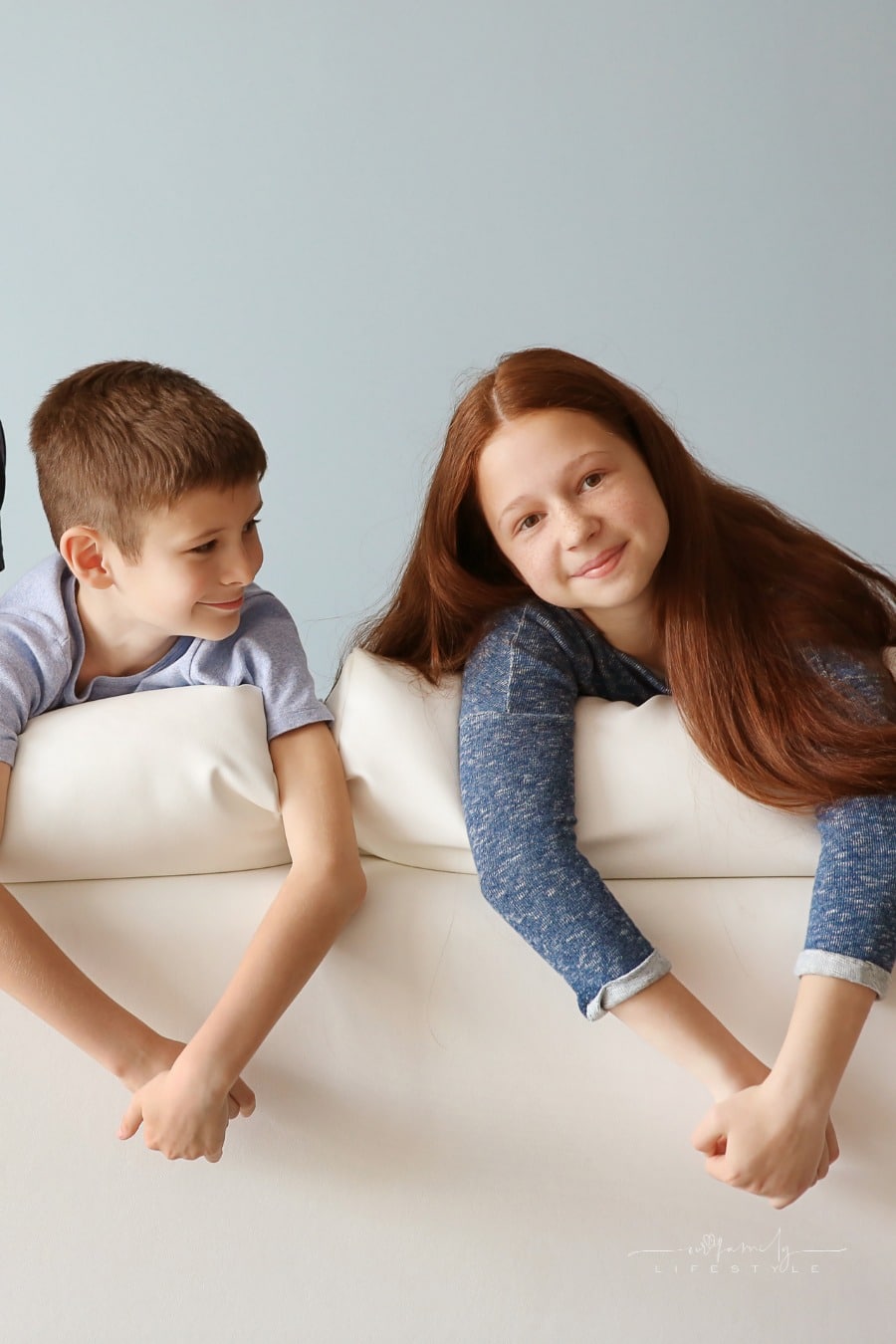 brother and sister smiling over back of couch