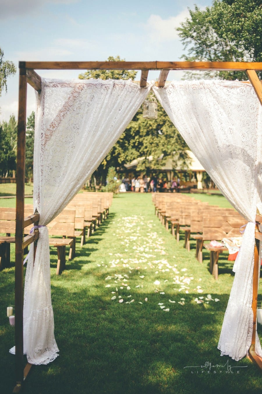 wedding arch with delicate lace curtain in front of wooden pews for outdoor garden wedding