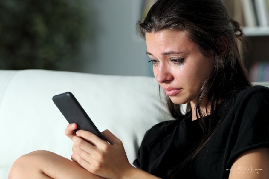 young female crying while reading cyberbully messages on phone