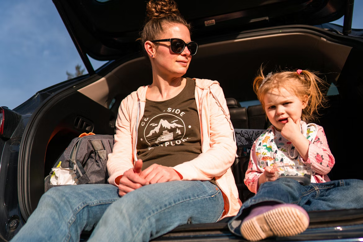 mother and young daughter sitting in car with open hatchback