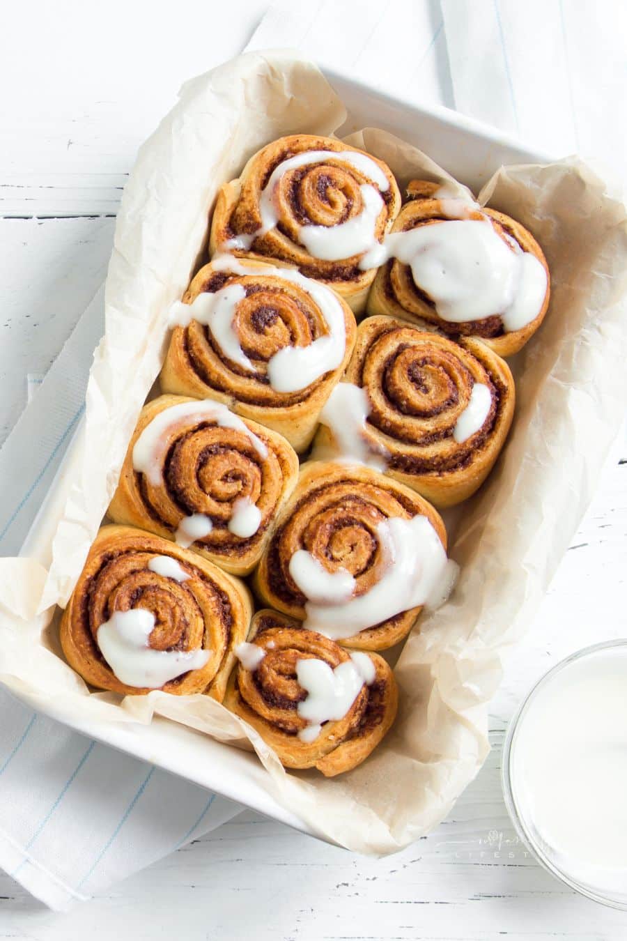 Cinnamon rolls or cinnabon, homemade sweet traditional dessert buns with white cream sauce on white wooden background, copy space.