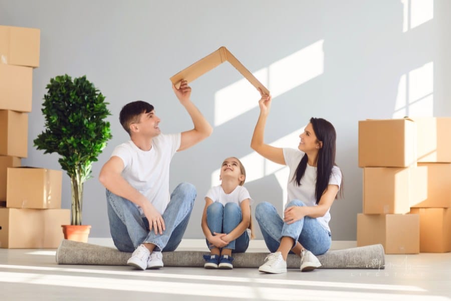 mom and dad holding a cardboard roof over daughter's head in new house