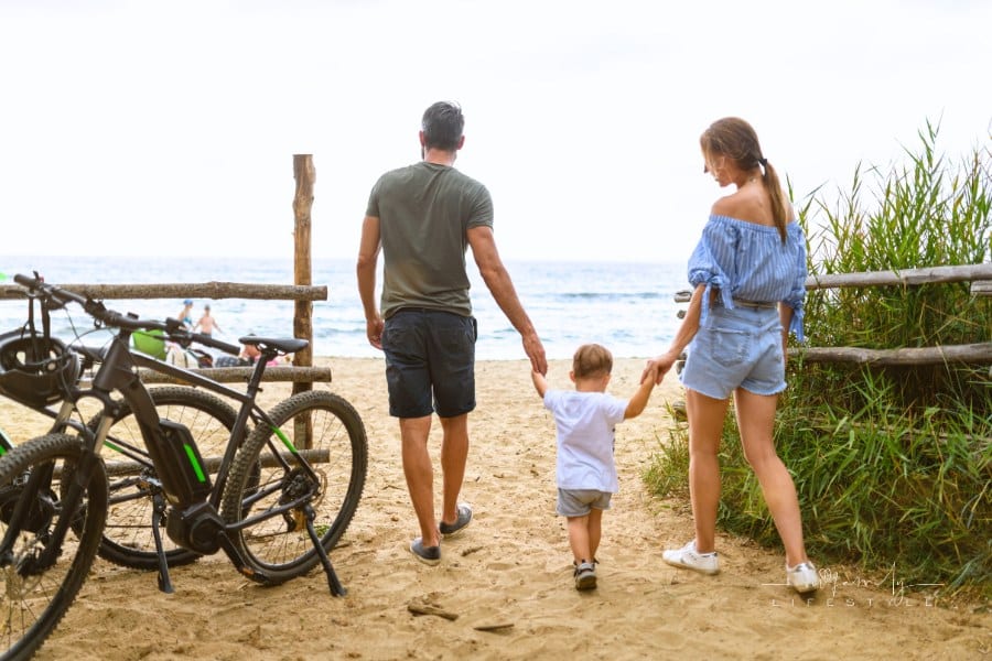 Family with toddler using e-bike in Tuscany entering beach, Italy