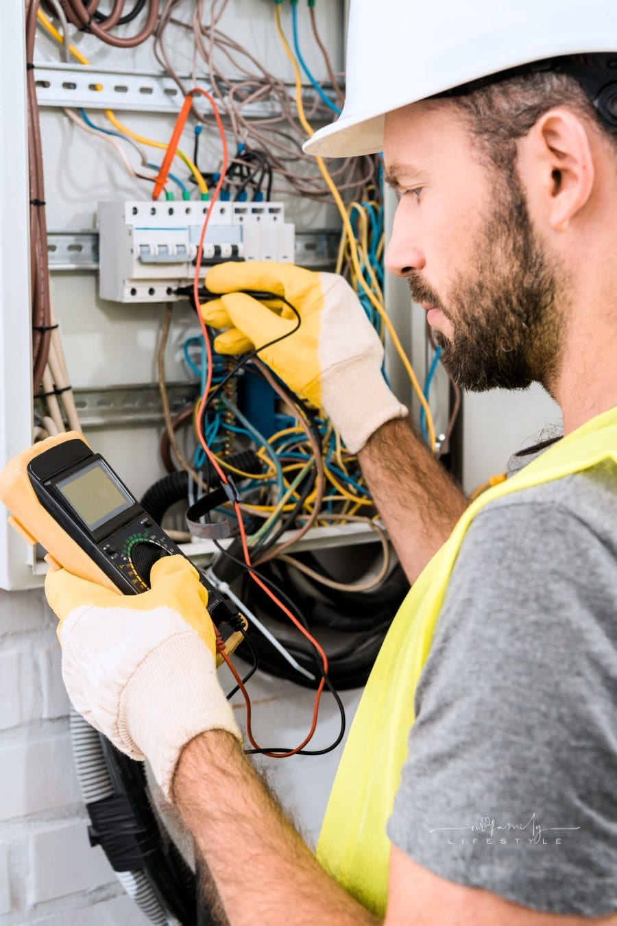 side view of bearded electrician checking electrical box with multimeter in corridor