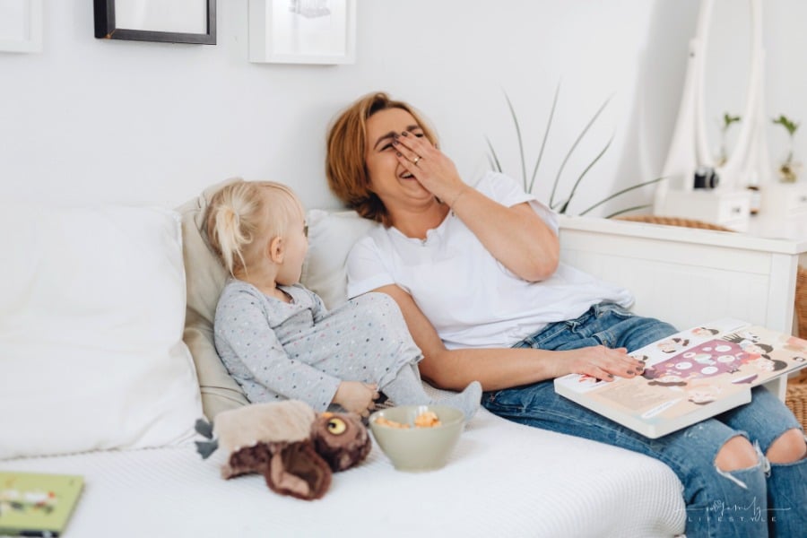 toddler and mom laughing while reading a book together on the couch