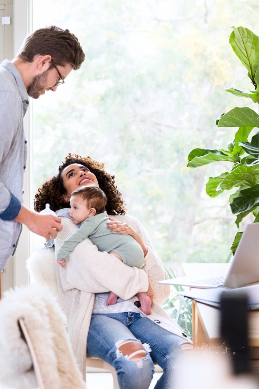 A young dad prepares to give a bottle to his newborn son. The man's wife is holding the baby and is working from an office in her home.