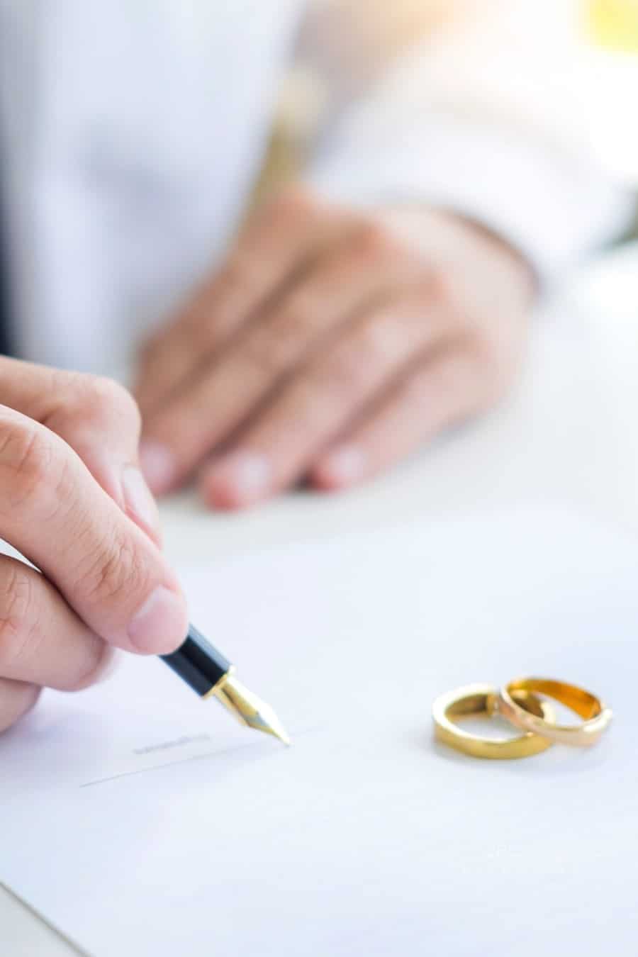 Man Signing Divorce Paper with Fountain Pen with Wedding Bands Lying Nearby