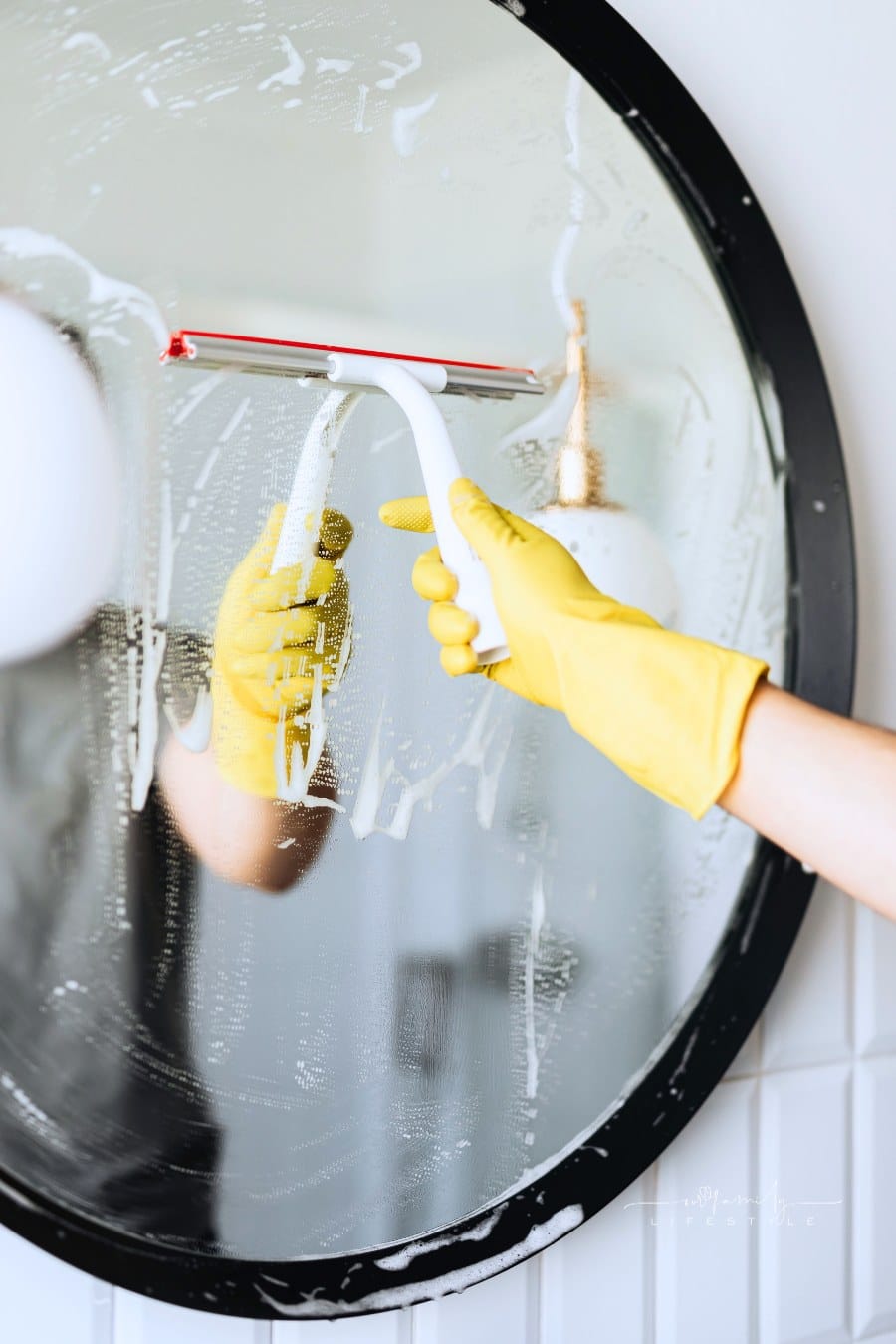 Unrecognizable person washing mirror in bathroom with squeegee