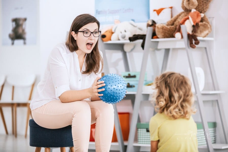 A sensory game with a blue ball played by a professional child therapist with a kid in a family support center.
