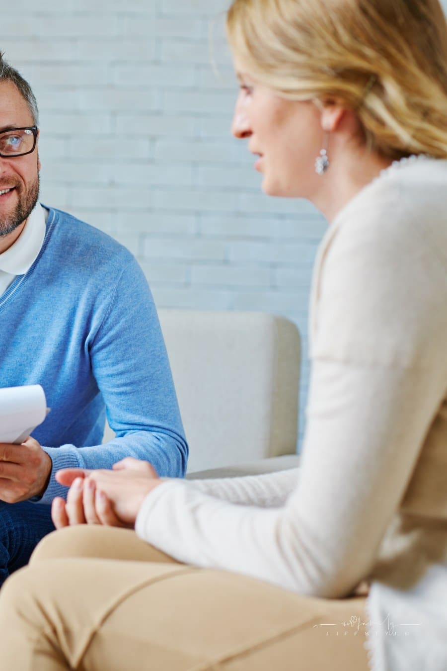 Bearded middle-aged psychologist having session with female patient and making notes in his private consulting room