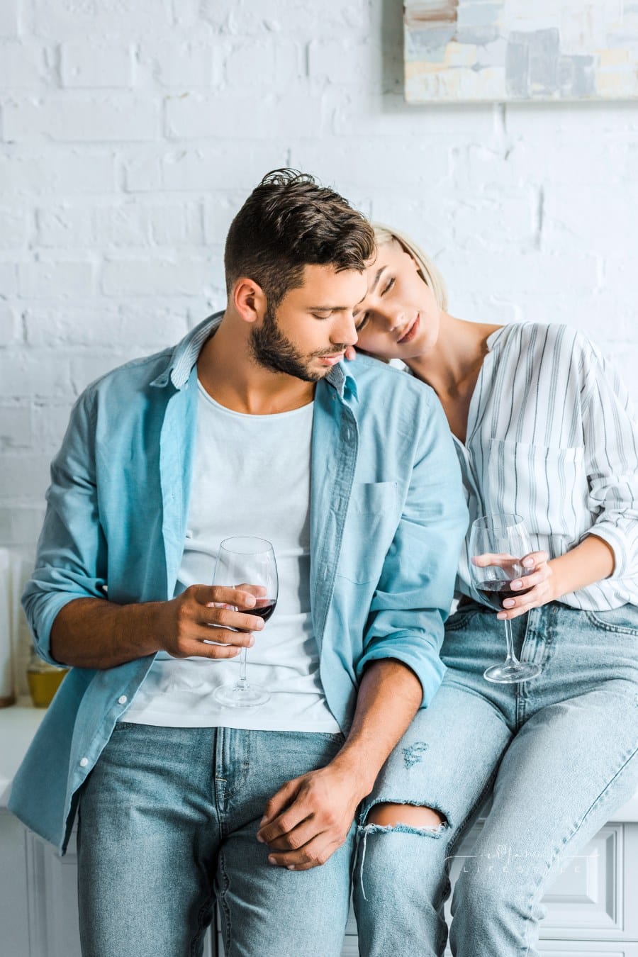 girlfriend holding glass of wine and leaning on handsome boyfriend in kitchen