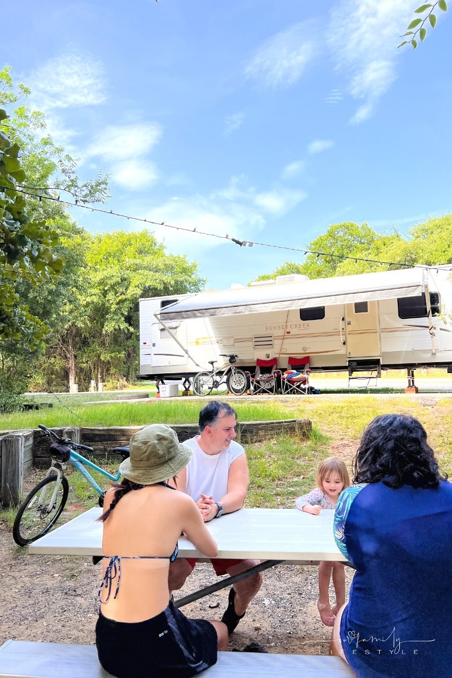 family sitting at picnic table in front of rv trailer and bikes