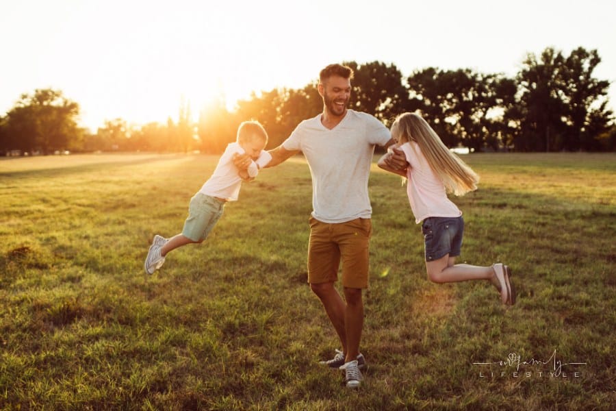 Happy looking father enjoying playing with his kids in a beautiful park at summer