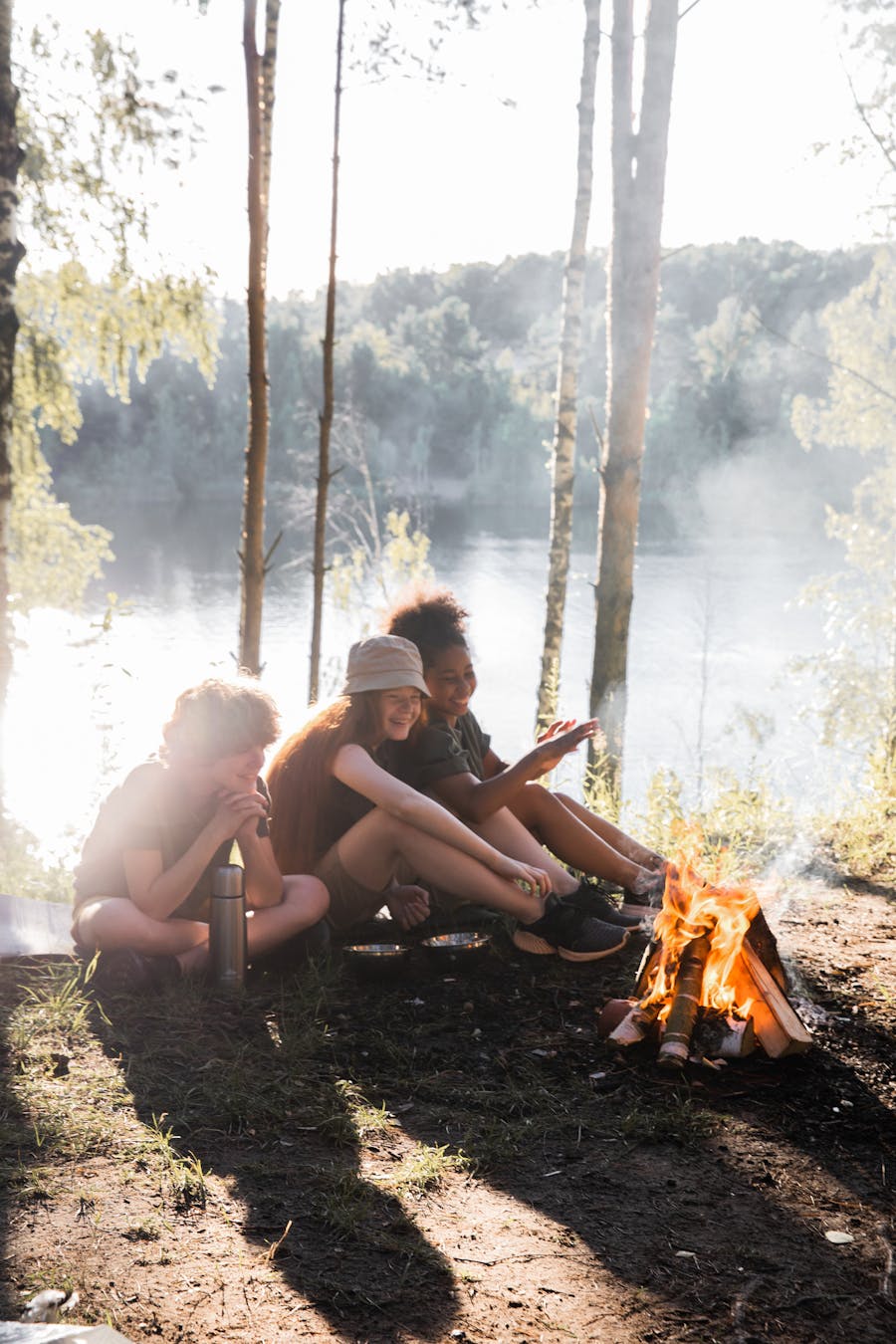 Group of children enjoying a campfire by a serene lake surrounded by nature.