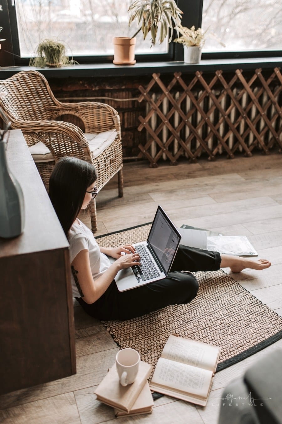 young woman typing on laptop surrounded by books on the floor