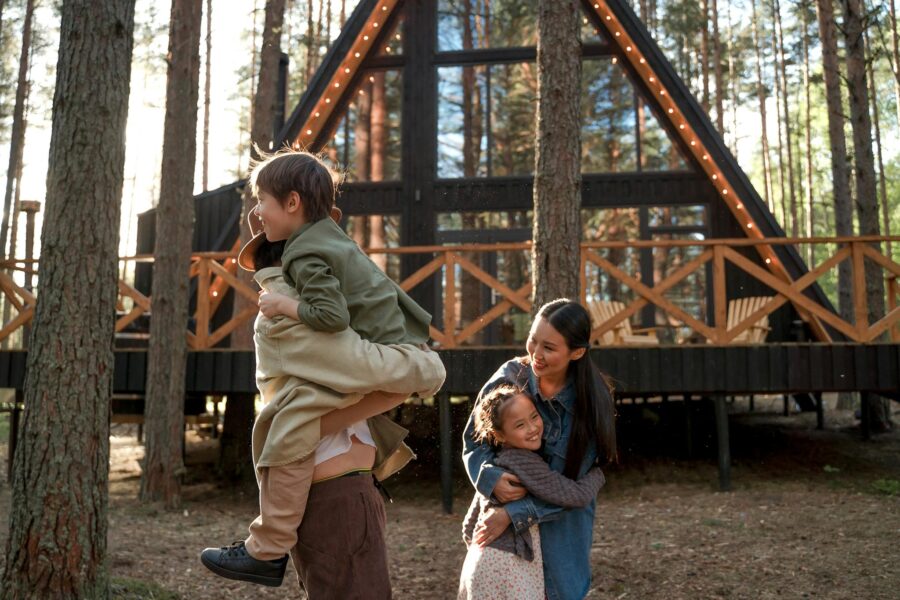 Happy family playing near a stylish A-frame cabin in a forest, enjoying outdoor time.