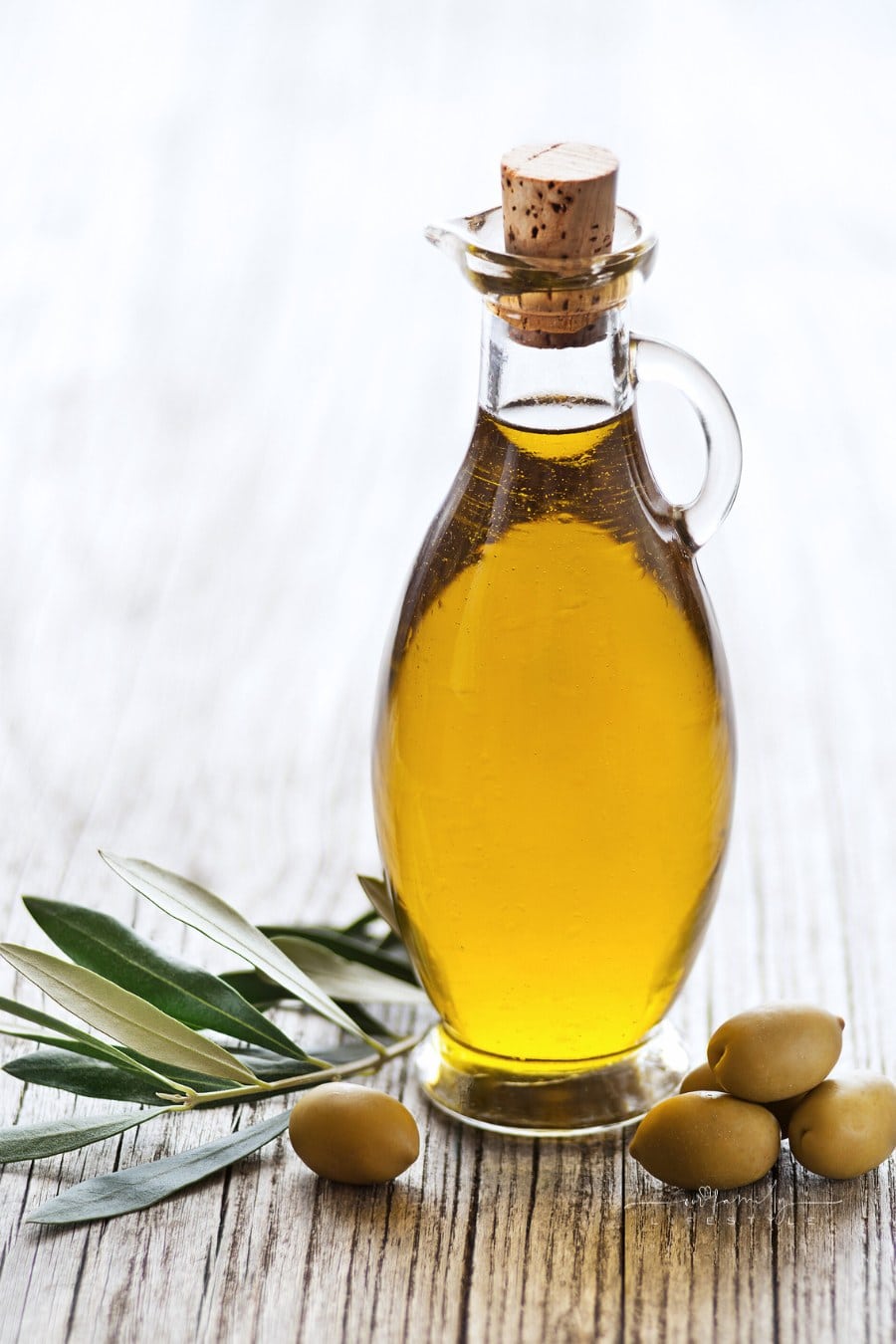 jar of olive oil with olive branch beside it on wooden table