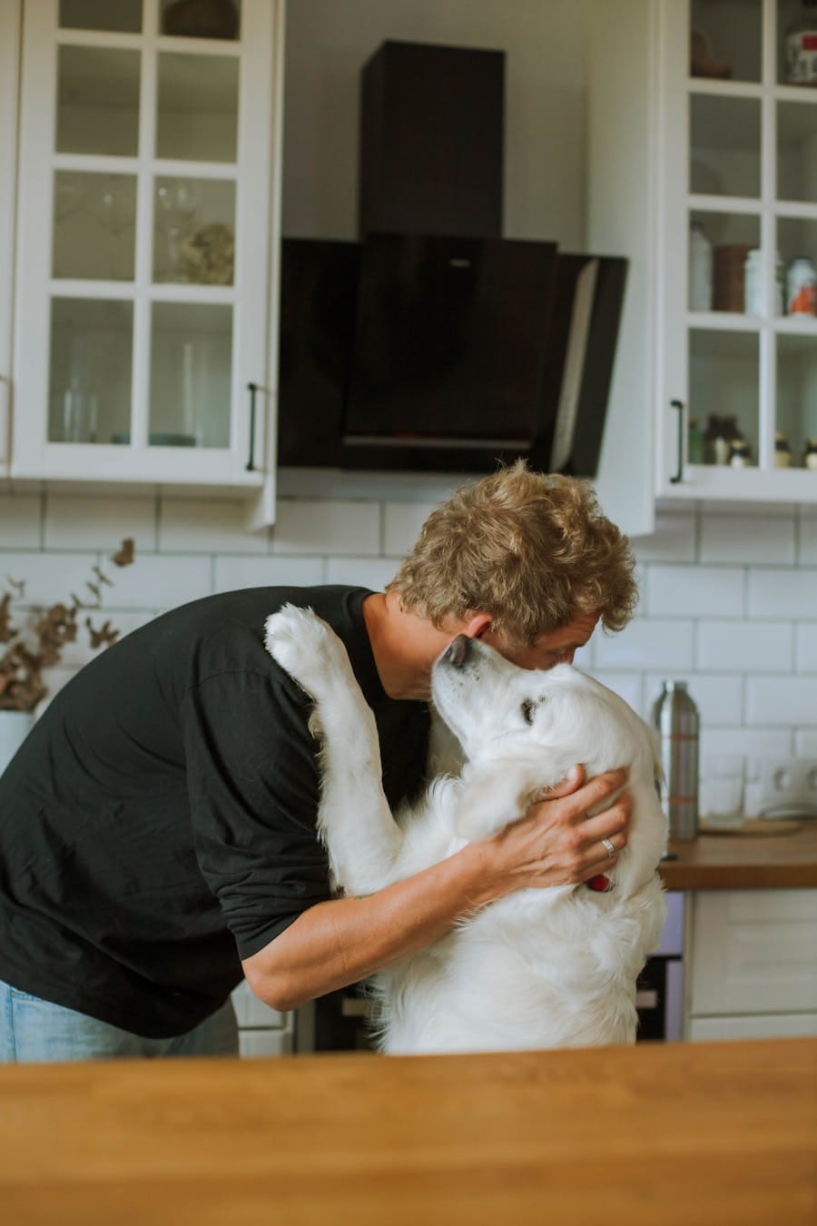 Heartwarming moment of a man hugging a dog in a cozy kitchen interior.
