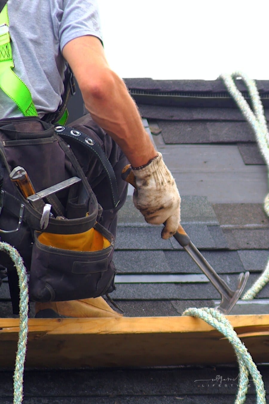 roofer wearing safety harness on a roof holding hammer