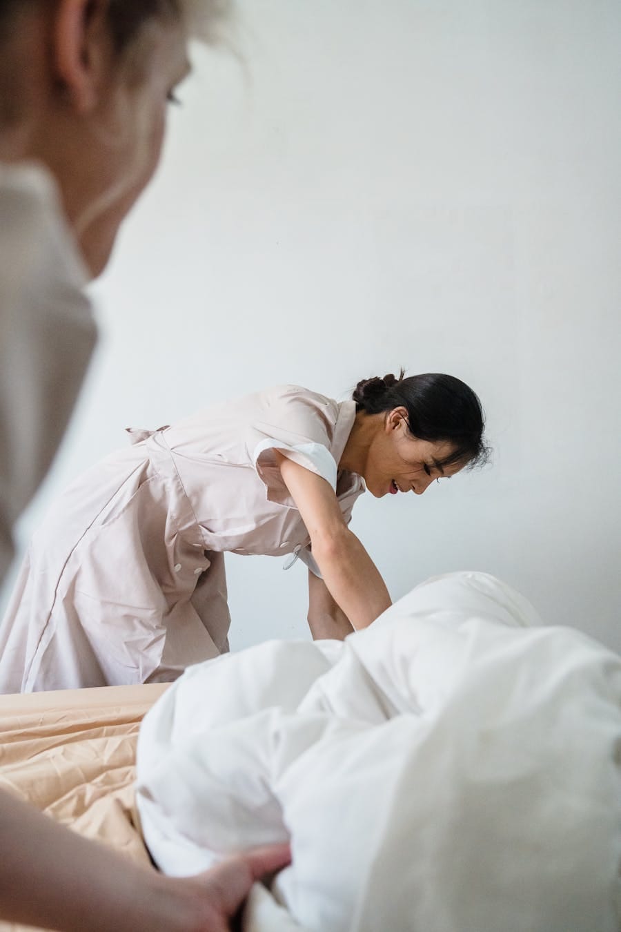 Housekeeper diligently making a bed with pristine white linens in a hotel room.