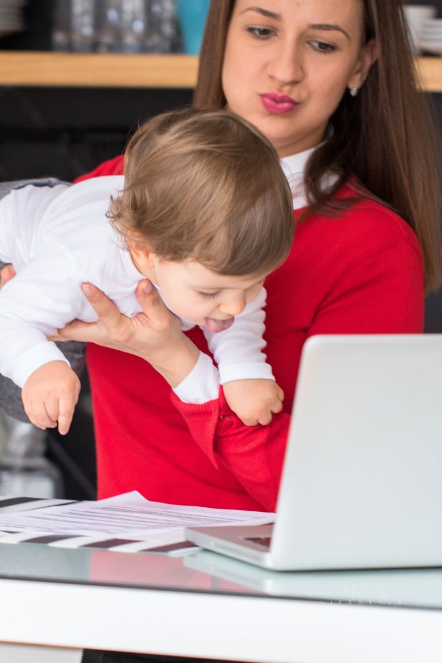 Single mother holding and playing with her baby girl while working on the kitchen bar