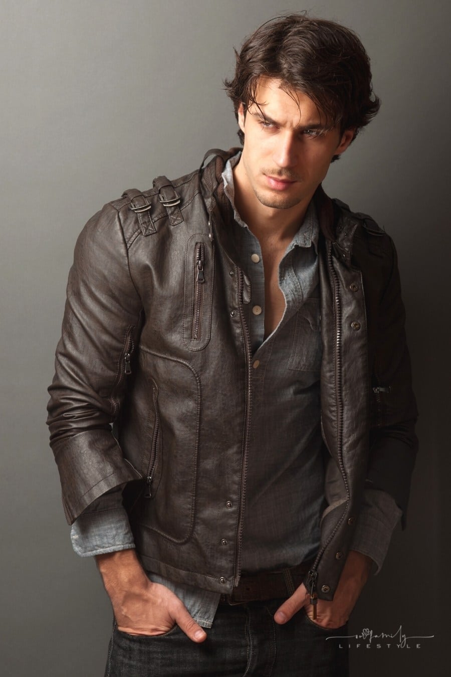 male model in leather jacket standing against a wall