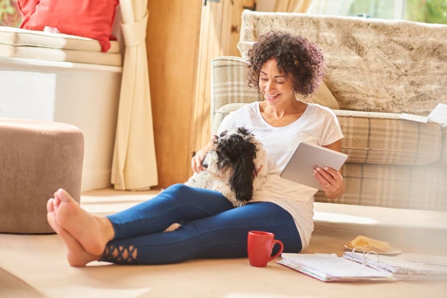 a woman sits in her lounge and browses on her digital tablet whilst sorting her paperwork with her dog