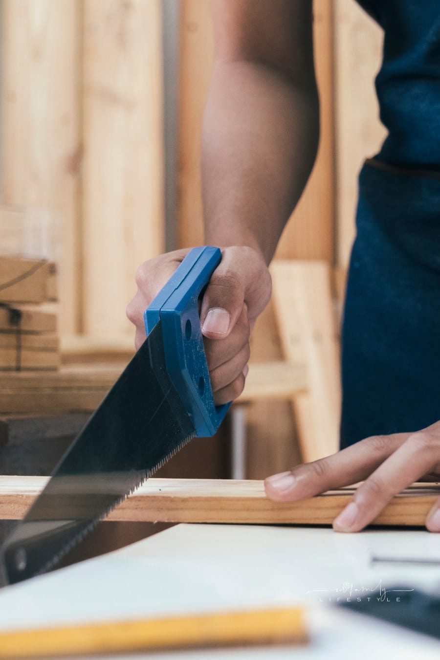 DIY Woodwork and Furniture Making; hand using saw to cut piece of wood