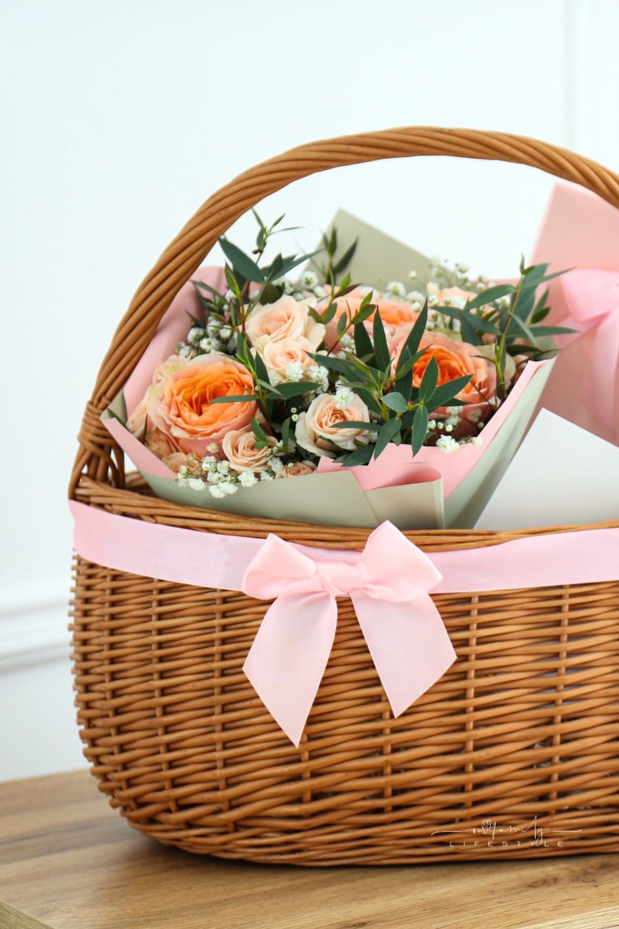 Wicker Basket with Pink Ribbon and Gifts on Table Indoors