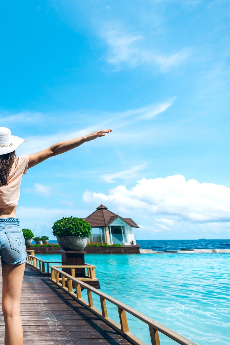 woman spreading her arms open on pier, in front of beach huts, on Maldives.