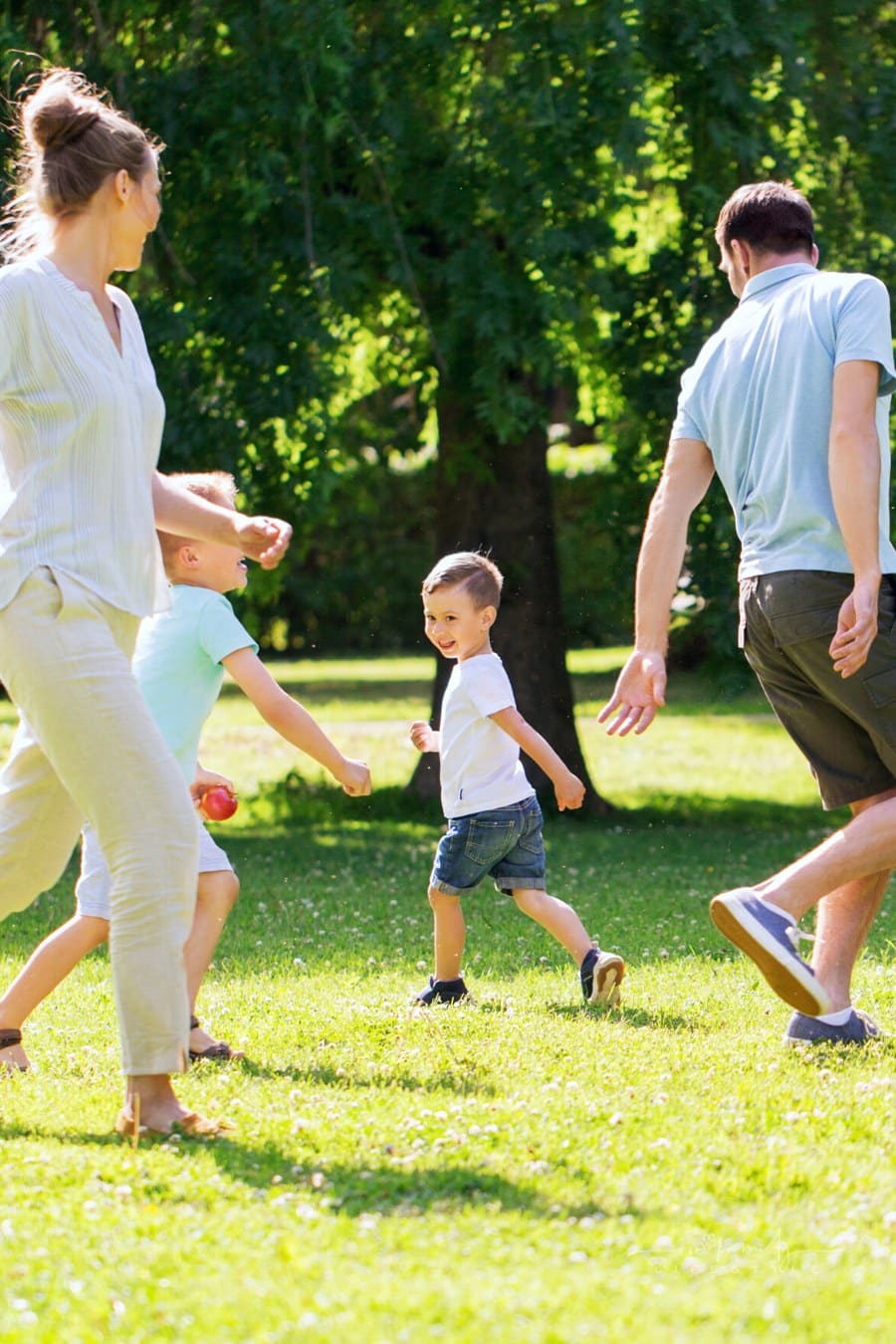 mom and dad playing chase with young sons outdoors