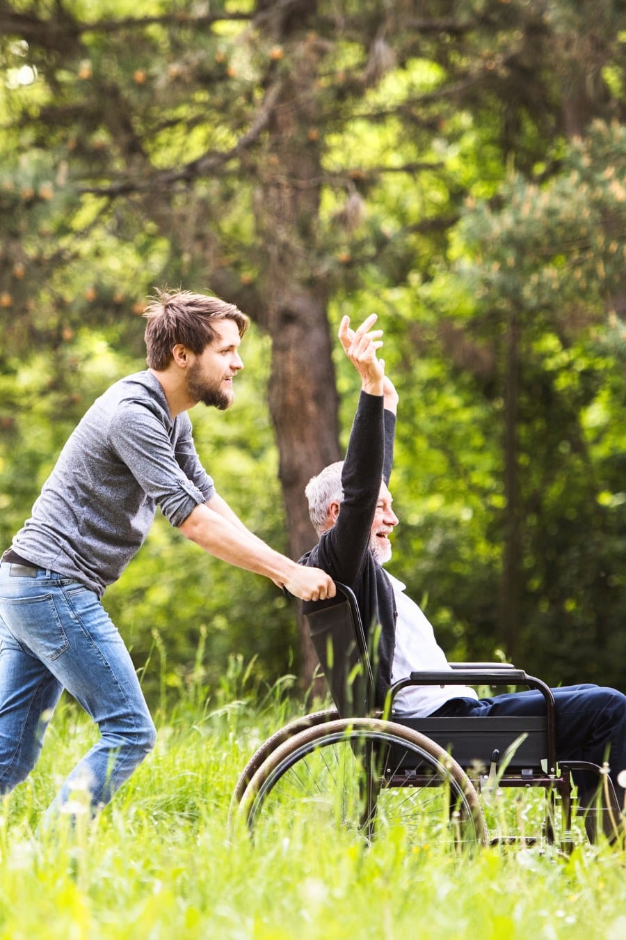 Hipster Son Walking with Disabled Father in Wheelchair at Park