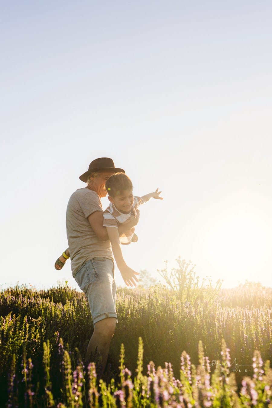 grandfather spinning his young grandson around in a field as if he his an airplane