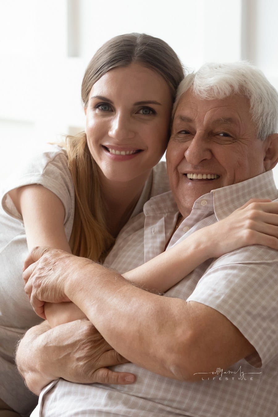 Adult daughter and elderly father embracing sitting on couch indoors