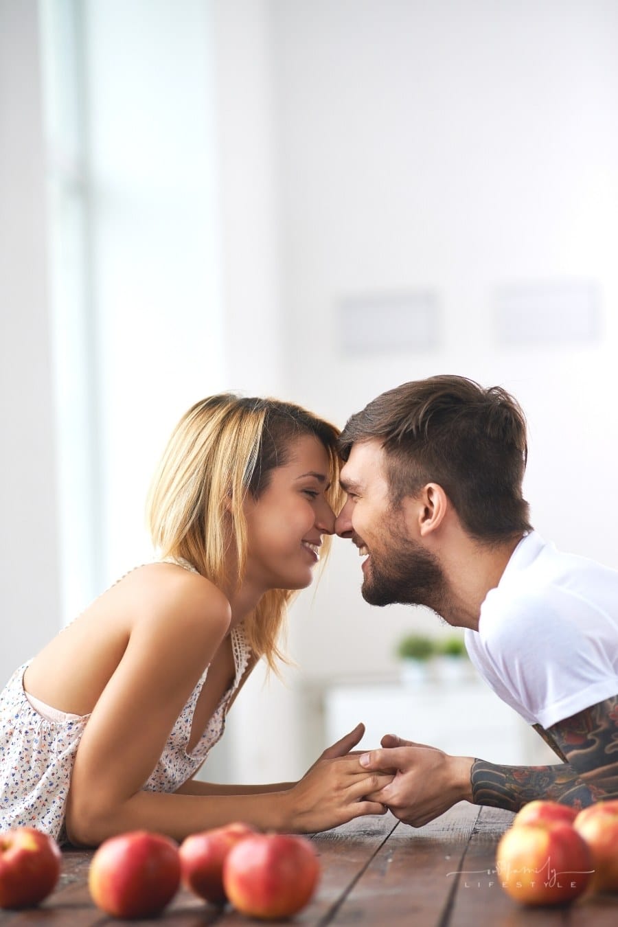 young couple holding hands with forehead together over a table covered in apples
