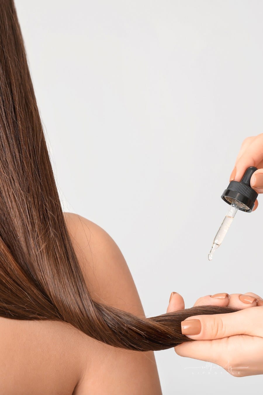 woman putting oil drops into long brown hair