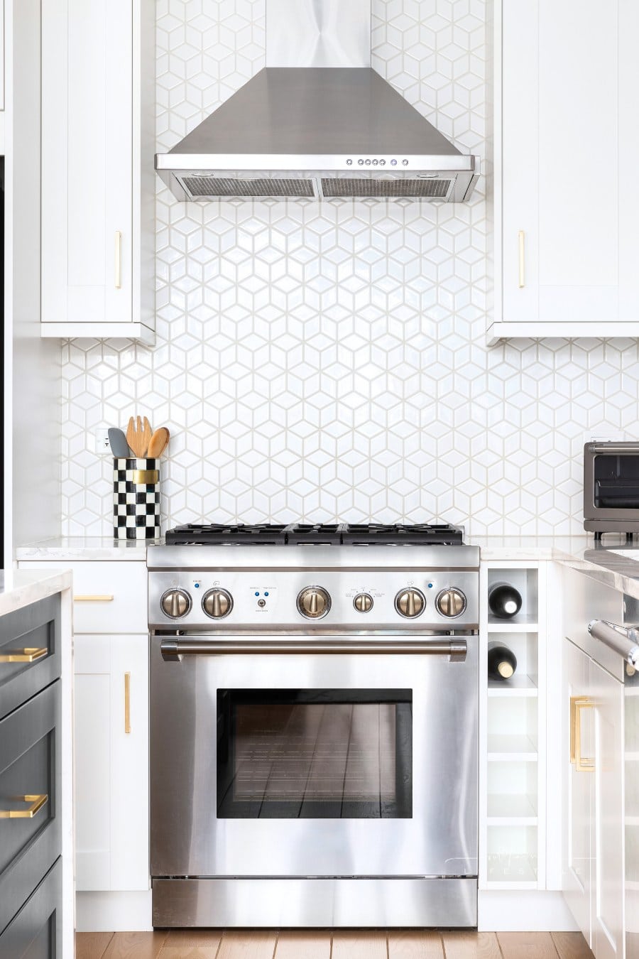 A stove detail with white cabinets and a tiled backsplash.