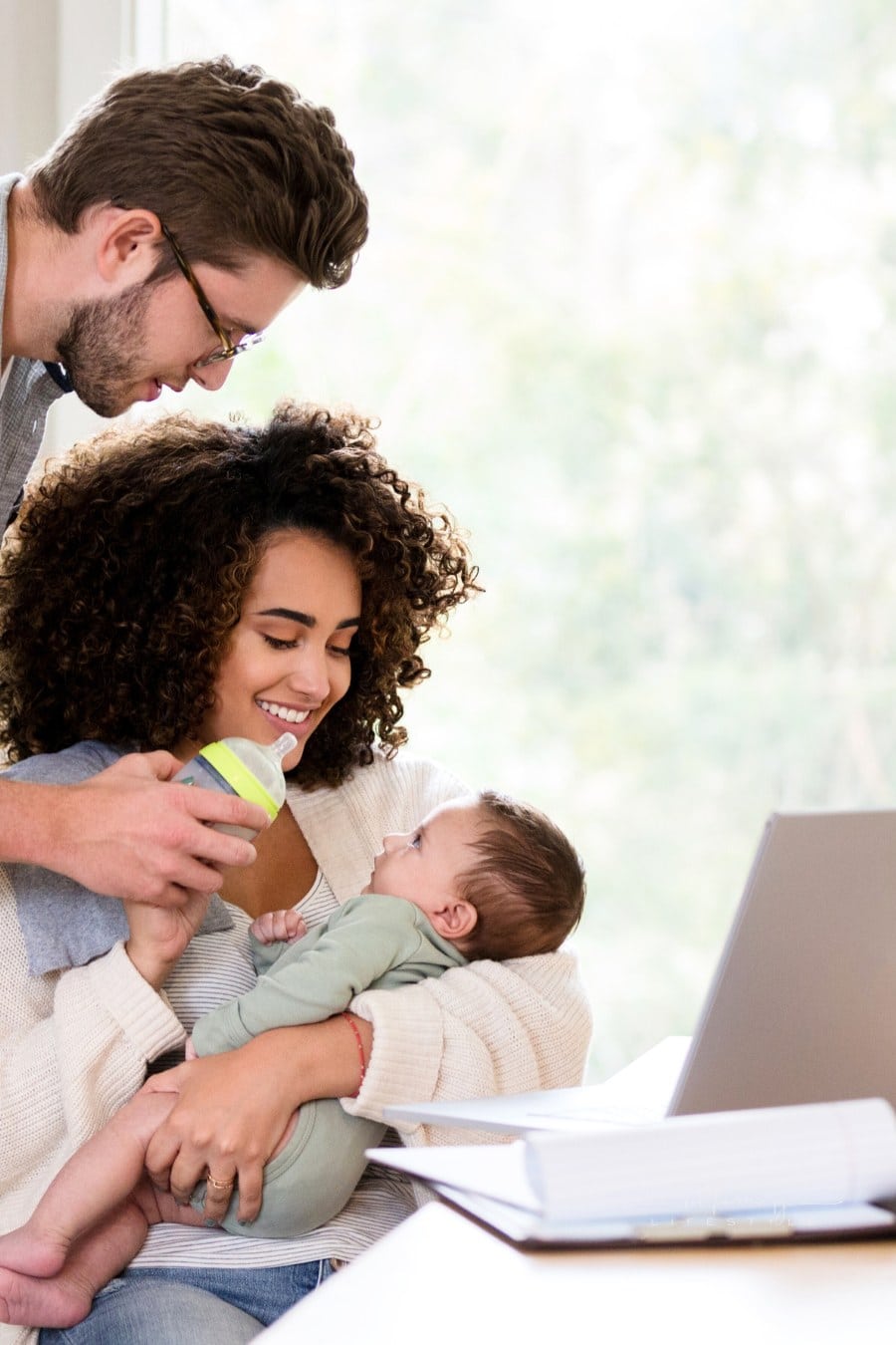 Young mom prepares to feed newborn son while dad stands behind her with bottle