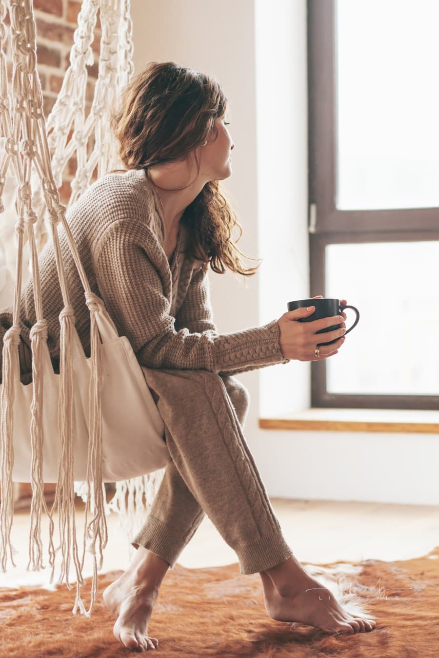 Woman Wearing Cashmere Nightwear Relaxing in indoor swing chair with a warm cup of coffee