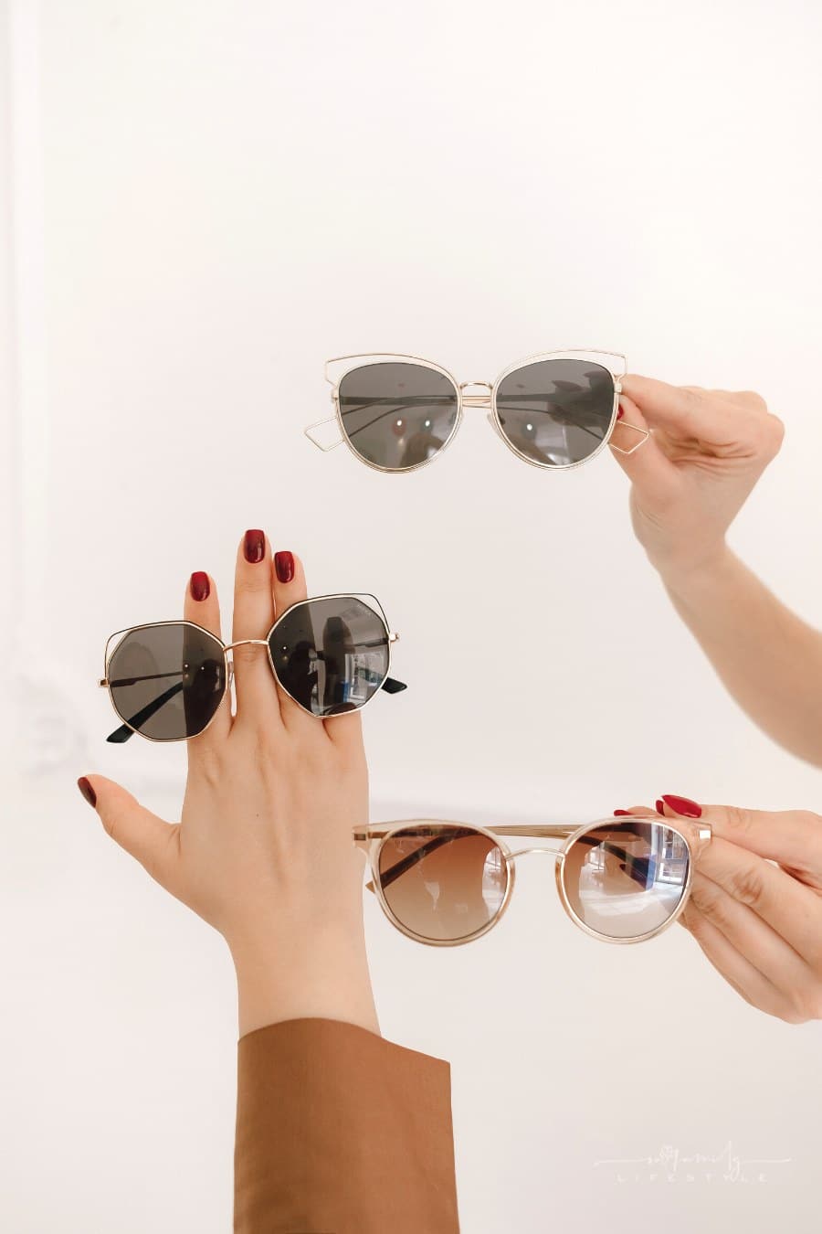women's hands holding up three pairs of sunglasses against white wall