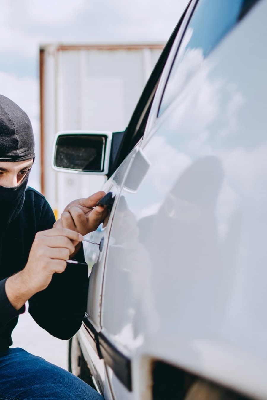 man dressed in black breaking into a parked car