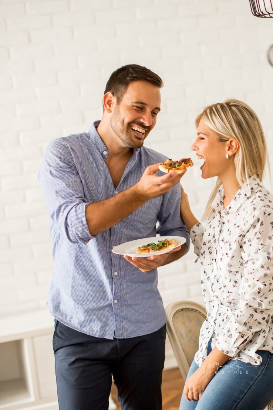 man feeding pizza to women as theh both laugh and smile