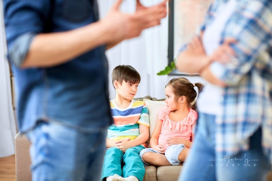 Young children sitting on couch while parents talk in front of them