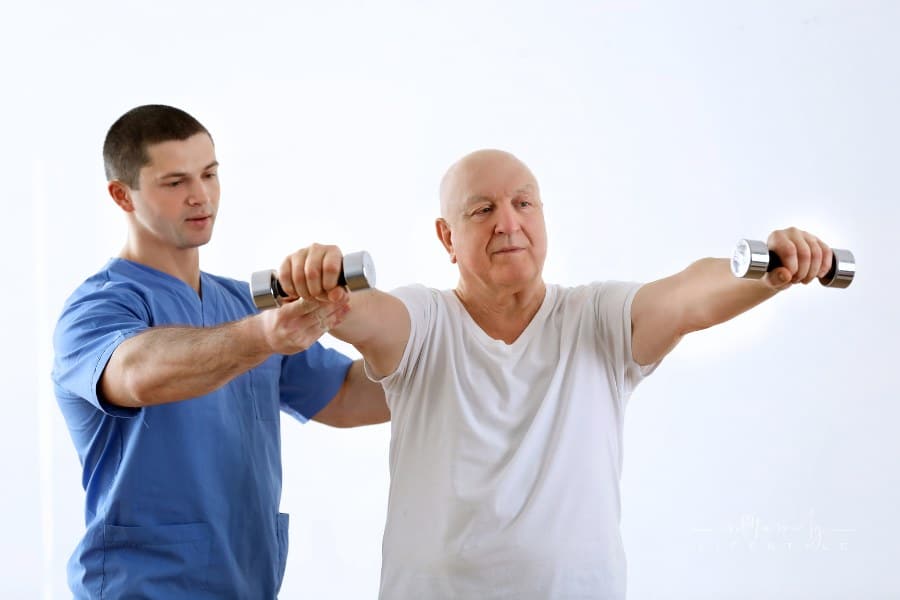 Physical therapist Assisting Elderly man with hand weights