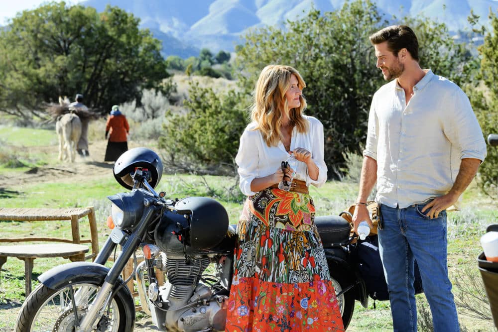 Laura Dern and Liam Hemsworth (cast members of Lonely Planet movie) standing beside a motorcycle in a rural setting, portraying Katherine and Owen during an outdoor moment in the Netflix film Lonely Planet.